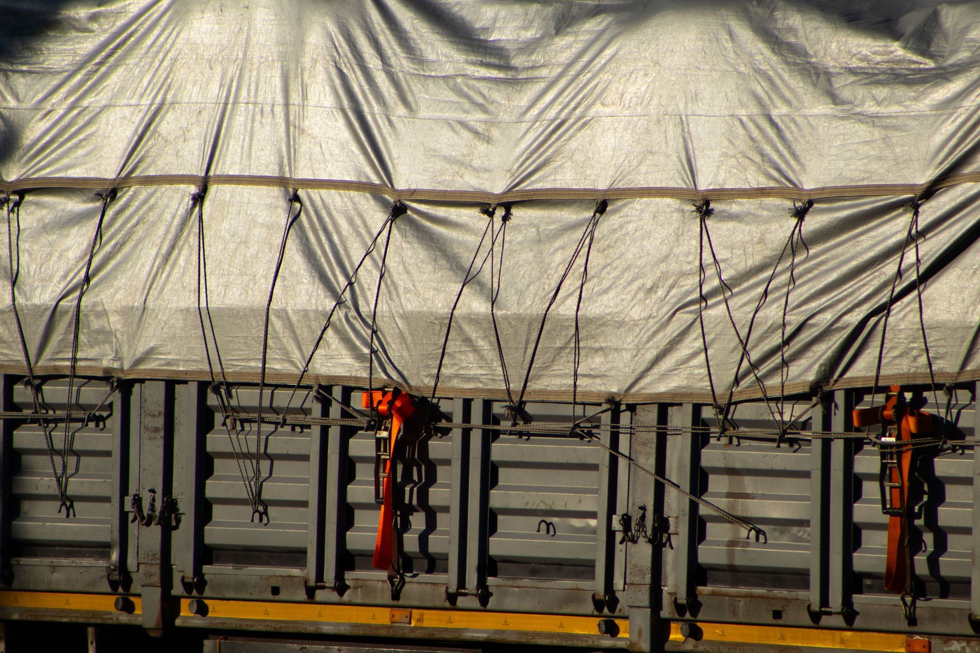 A cargo truck covered with a secured tarp fastened by ropes and straps over metal side panels