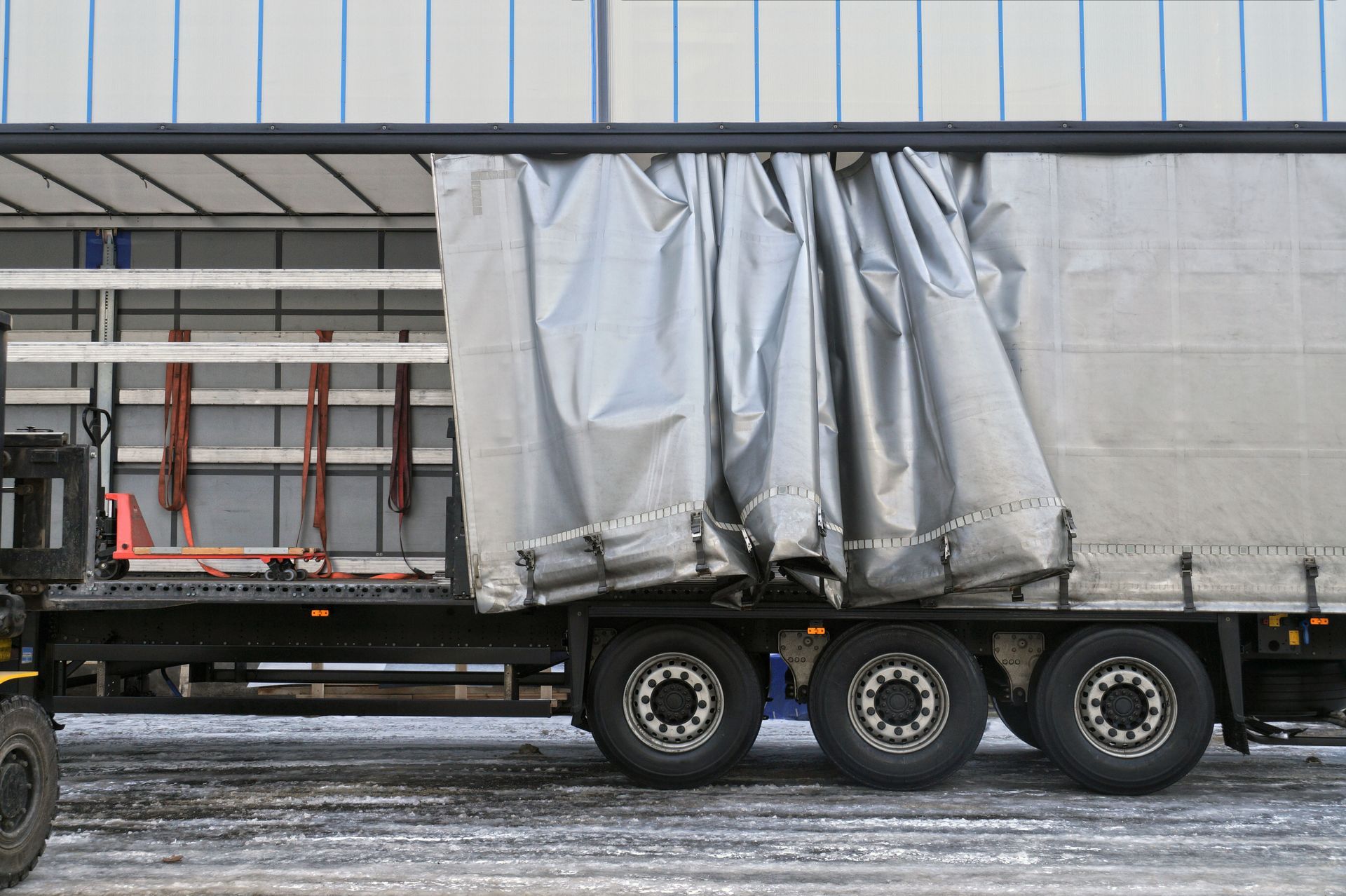 Side view of a truck with its tarp pulled open, revealing the empty cargo area.