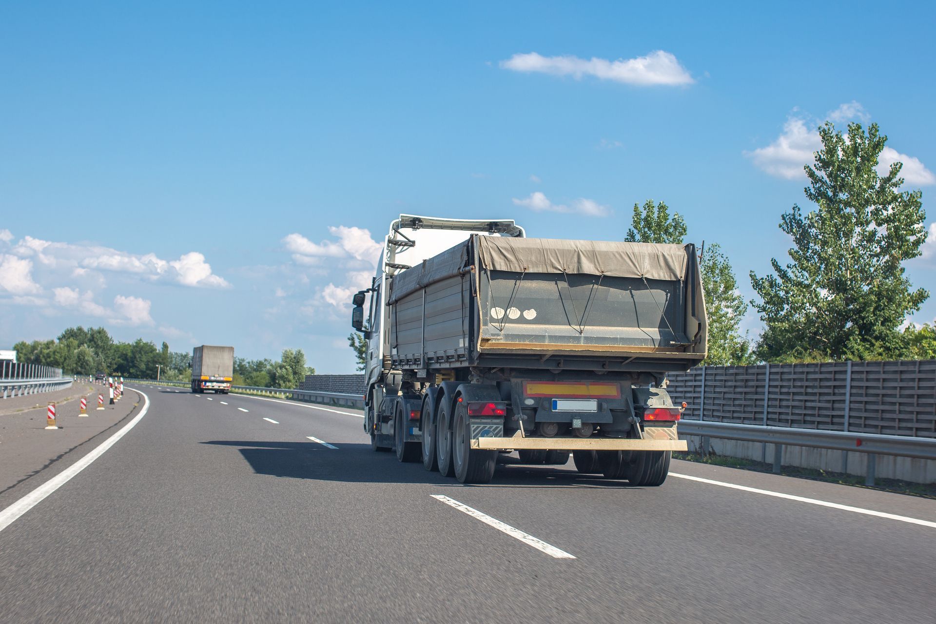 Truck driving on a highway with a tarp covering its cargo bed on a clear, sunny day.