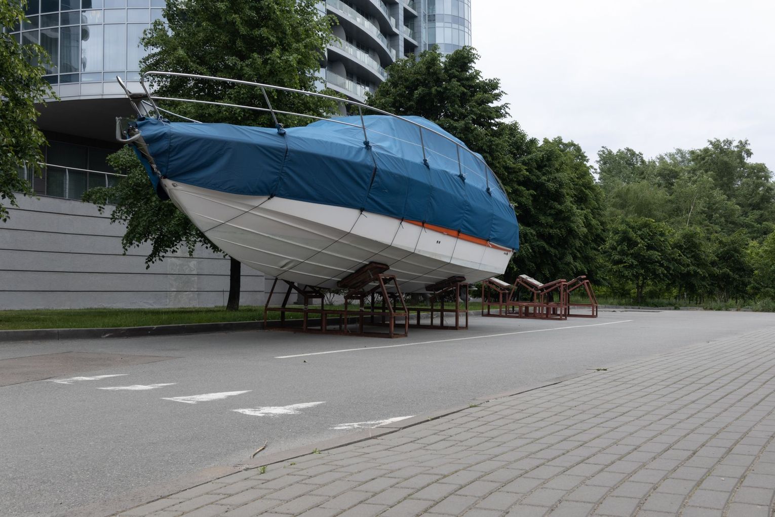 The boat is protected by a durable tarp system while in outdoor storage on a city street.