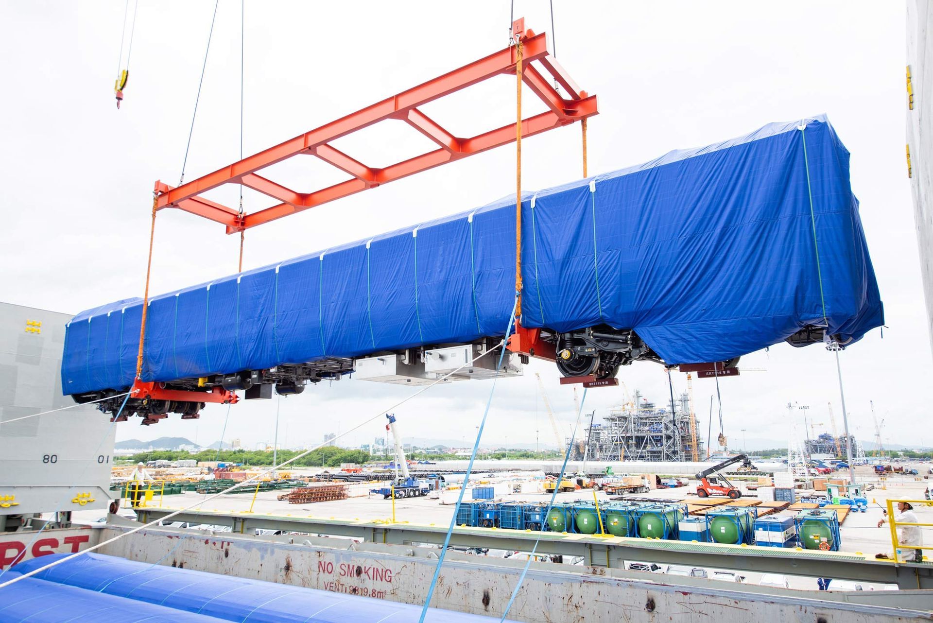 Unloading operation of project cargo covered in industrial tarp with port heavy lift cranes.