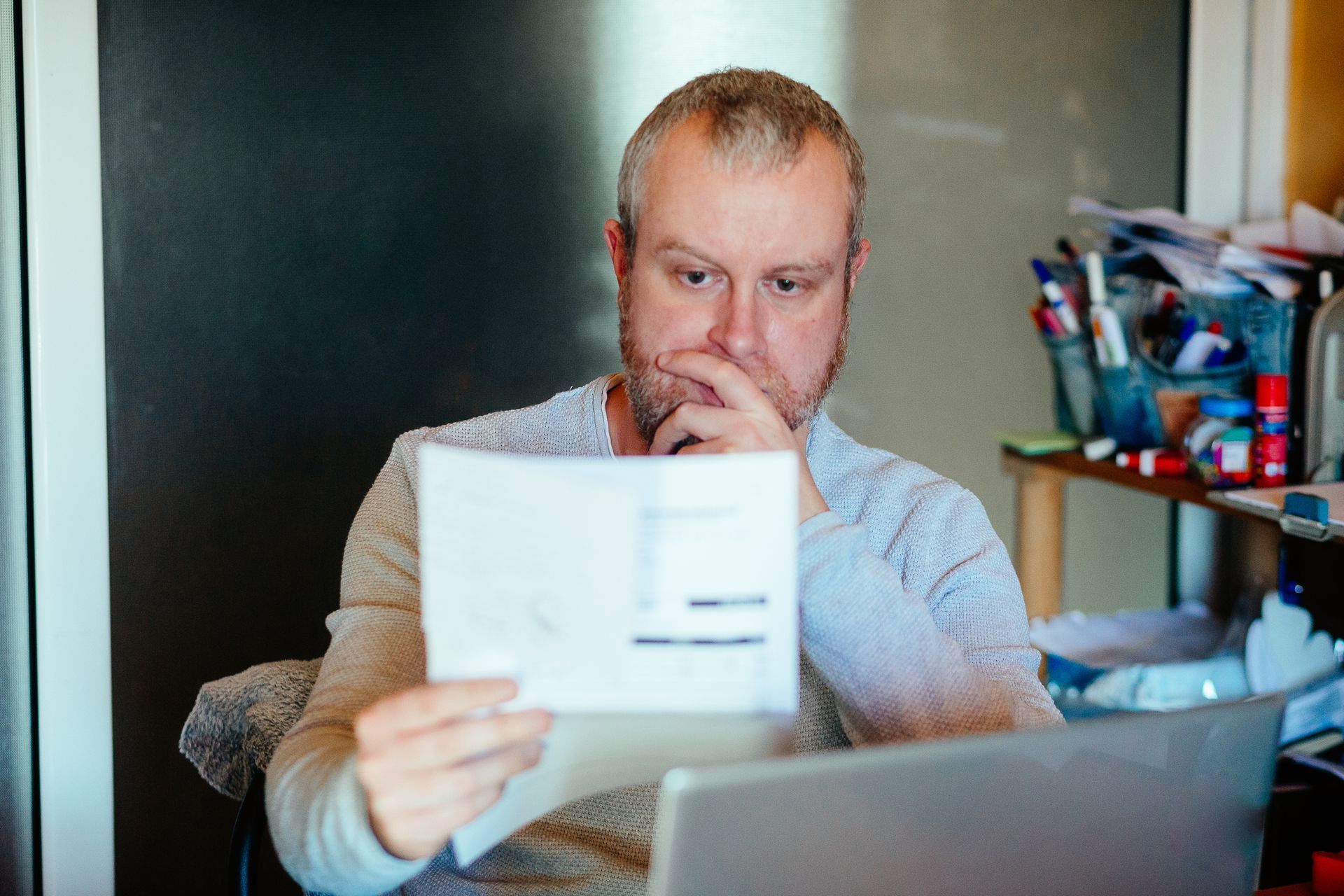 A worried homeowner looking at high heating bills while sitting near a thermostat in their New Roche