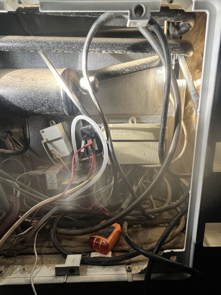 The inside of a refrigerator with a lot of wires coming out of it.