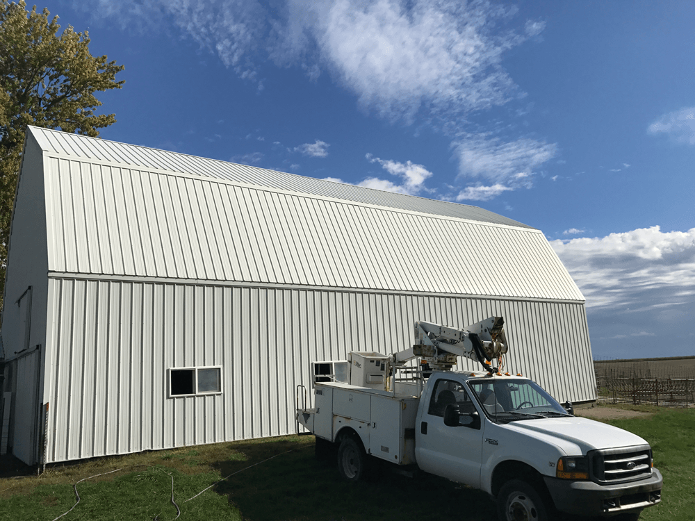 White barn with a white utility truck parked in front, under a blue sky.