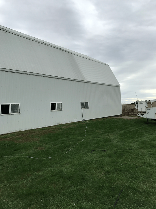 White barn with small windows on green grass under a cloudy sky.