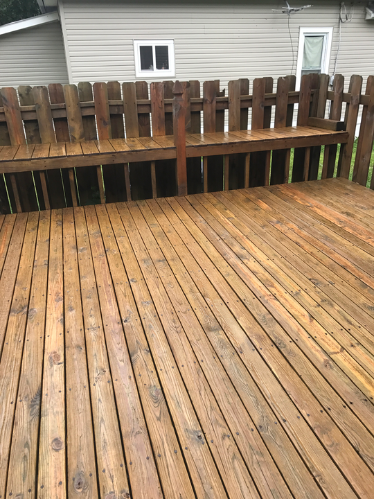 Wooden deck with a built-in bench and a wooden fence in front of a house.