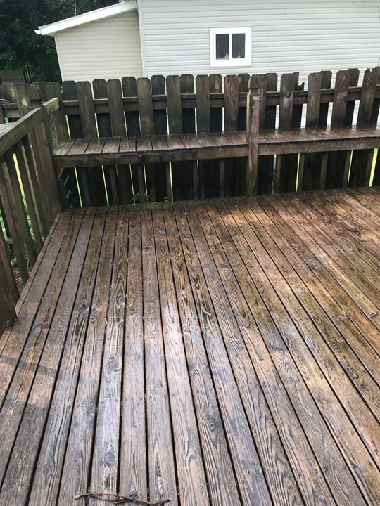 Wooden deck with fence and shed in the background; wet with a dark stain.
