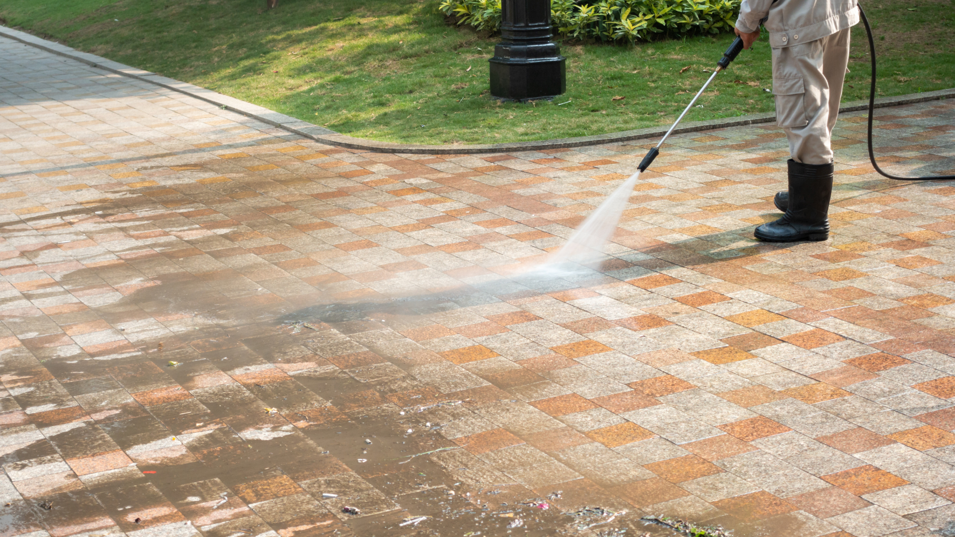 Person pressure washing a brick paved walkway in an outdoor setting.