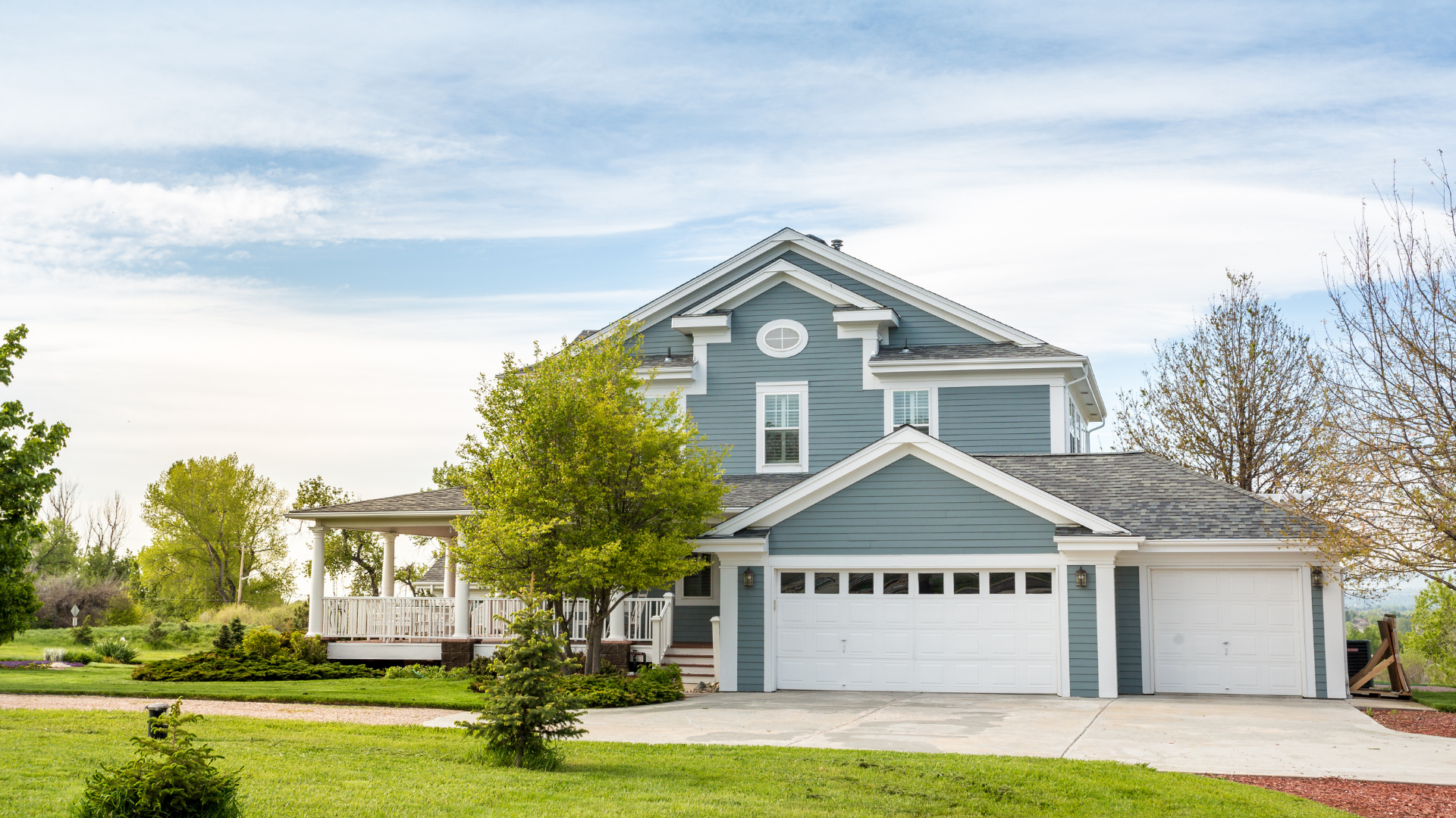 Two-story blue house with a white garage and a green lawn under a cloudy sky.