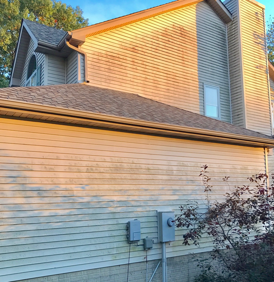 Beige siding on a house with a brown roof, lit by the sun.