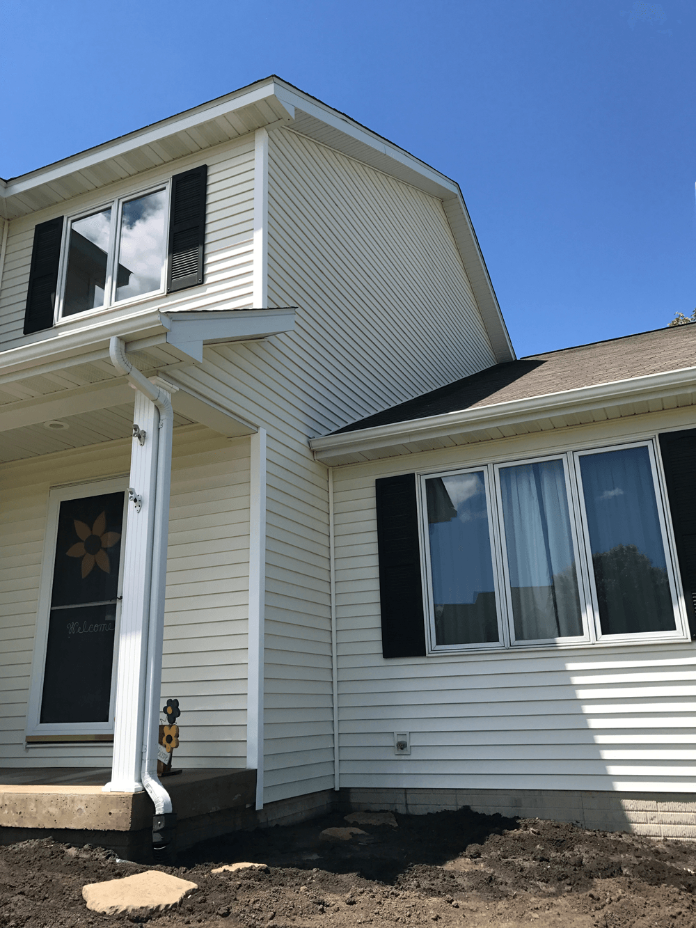 Two-story house with white siding, black shutters, and a dark roof under a clear blue sky.