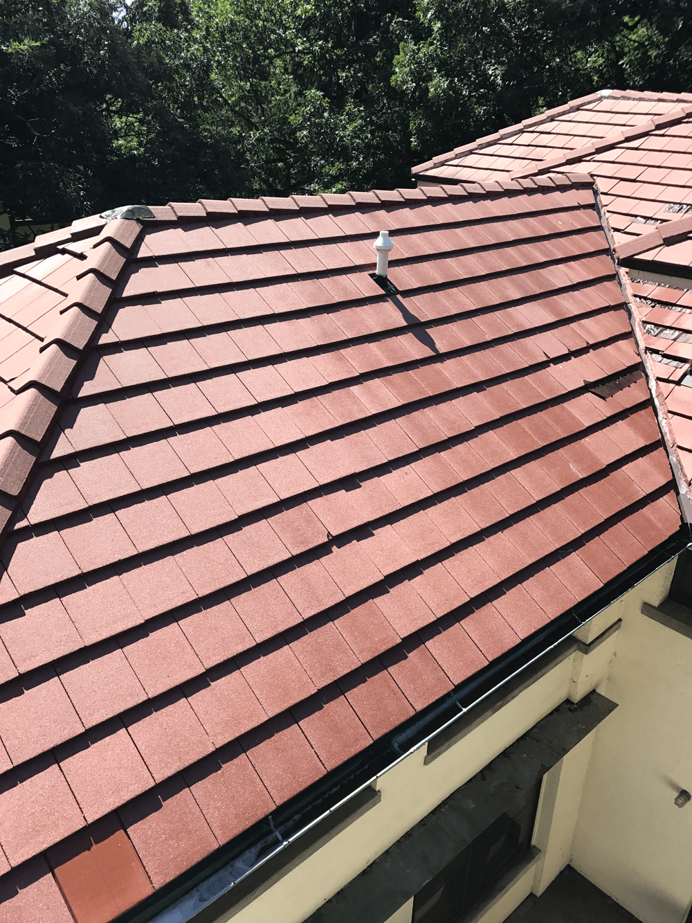 Red tiled roof with a vent pipe, set against a backdrop of green trees.