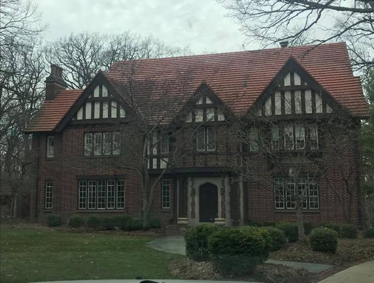 Two-story Tudor home with red brick, a brown tile roof, and white accents.