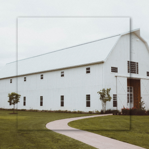 White barn with a long, curved path leading to the entrance, on a grassy lawn under a cloudy sky.