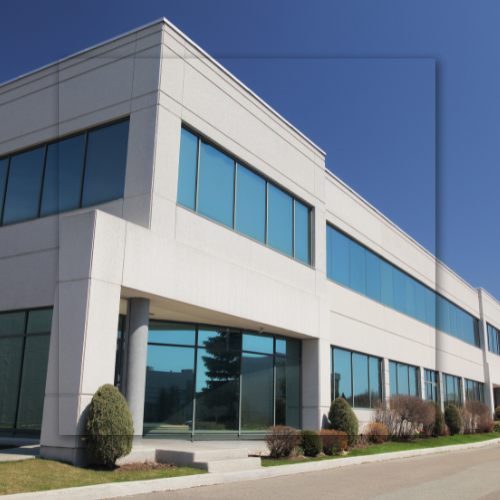 Modern white two-story office building with blue-tinted windows. Clear blue sky backdrop.