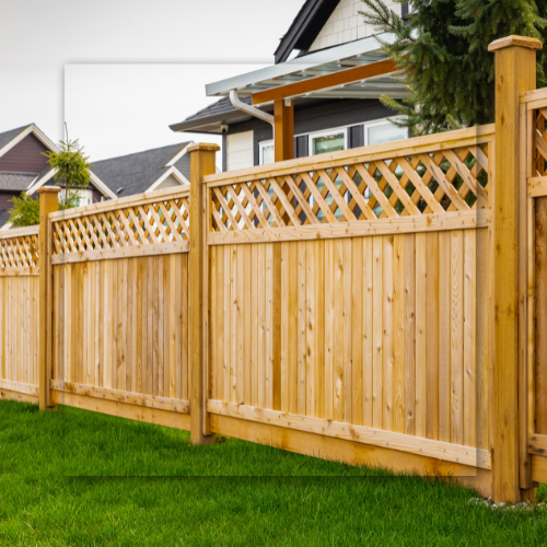 Wooden fence surrounding a green lawn, with a house in the background.