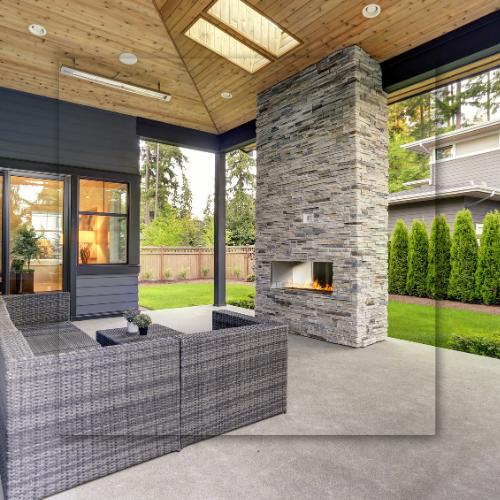Outdoor patio with gray sofa, fireplace, and lush greenery.