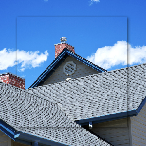 House roof with gray shingles, brick chimney, and blue sky with white clouds.