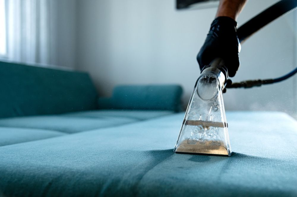 A person is cleaning a blue couch with a vacuum cleaner.
