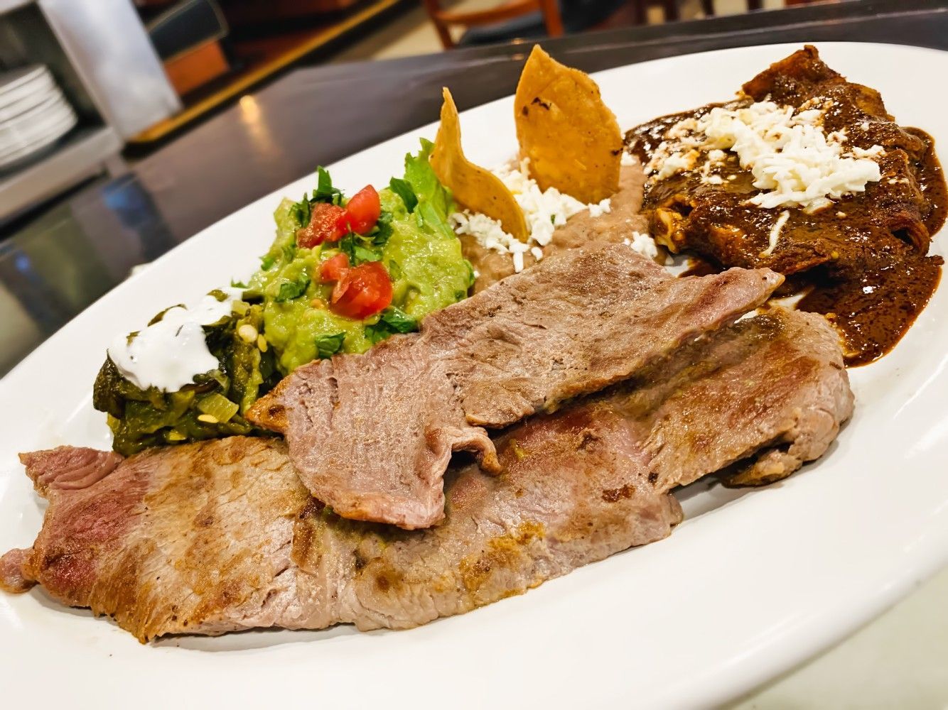 A white plate topped with meat , guacamole and tortilla chips.