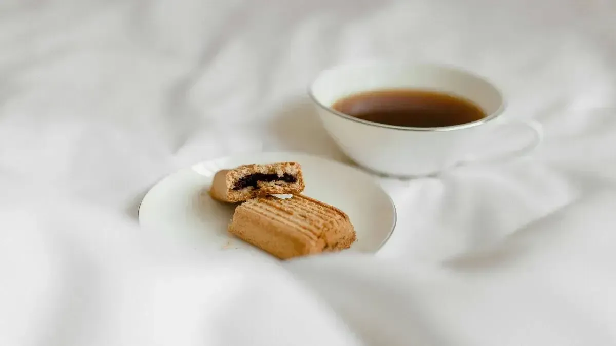 A cup of coffee and a plate of cookies on a bed.
