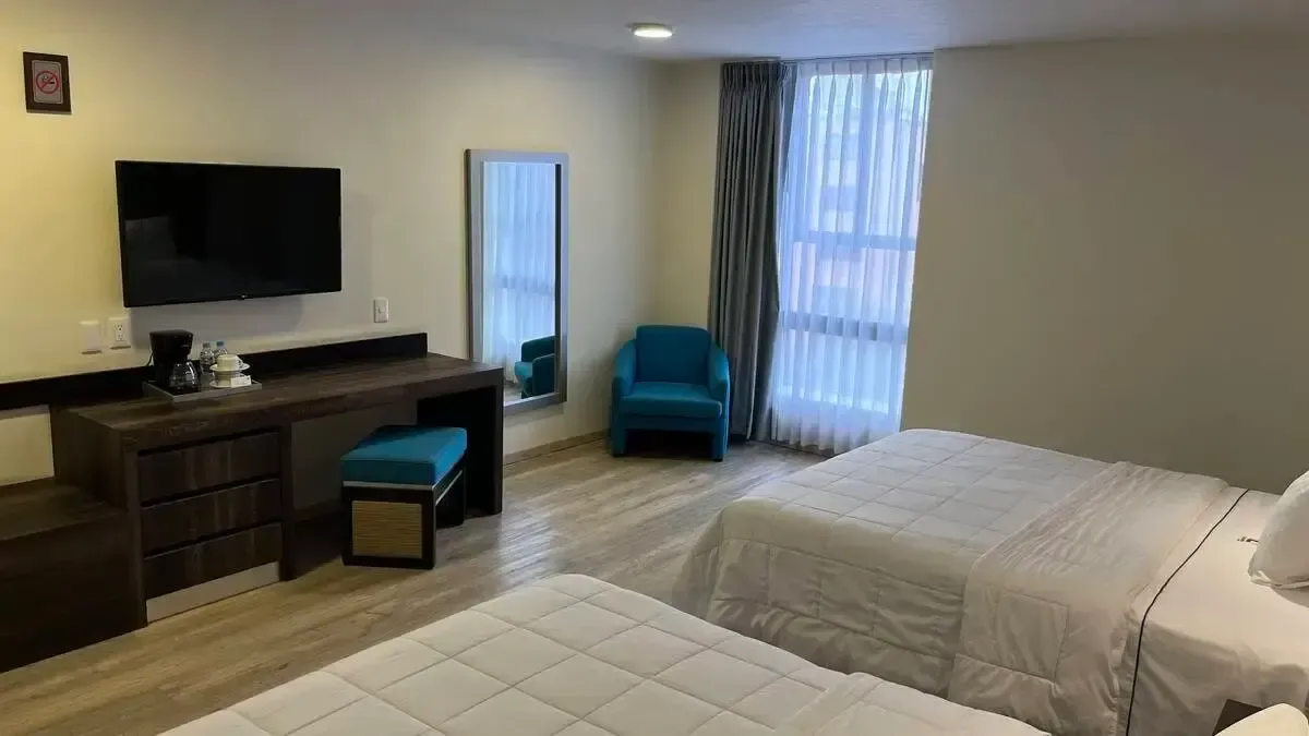 A hotel room with two beds , a chair , a desk and a flat screen tv.