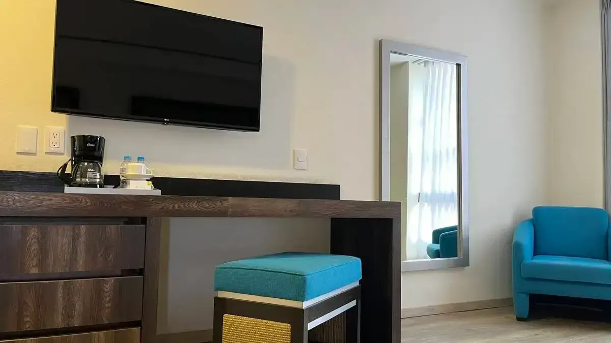 A hotel room with a desk , chair , television and mirror.