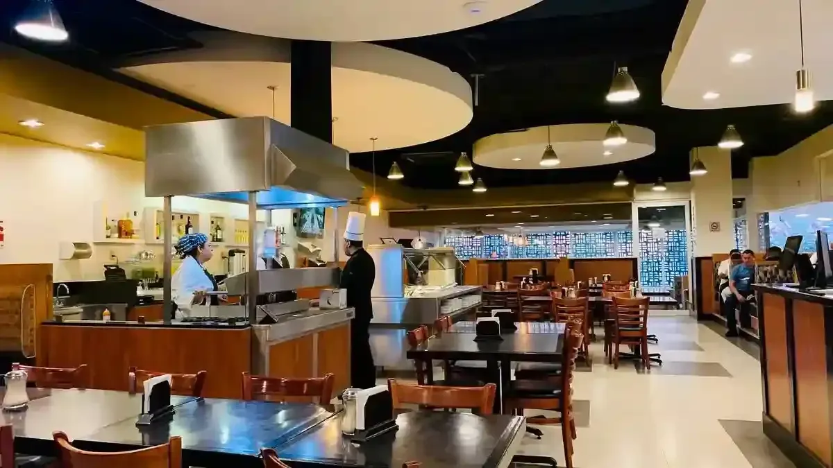A restaurant with tables and chairs and a chef in the kitchen.