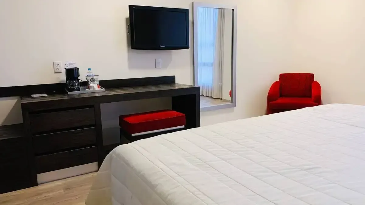 A hotel room with a bed , chair , desk , television and mirror.