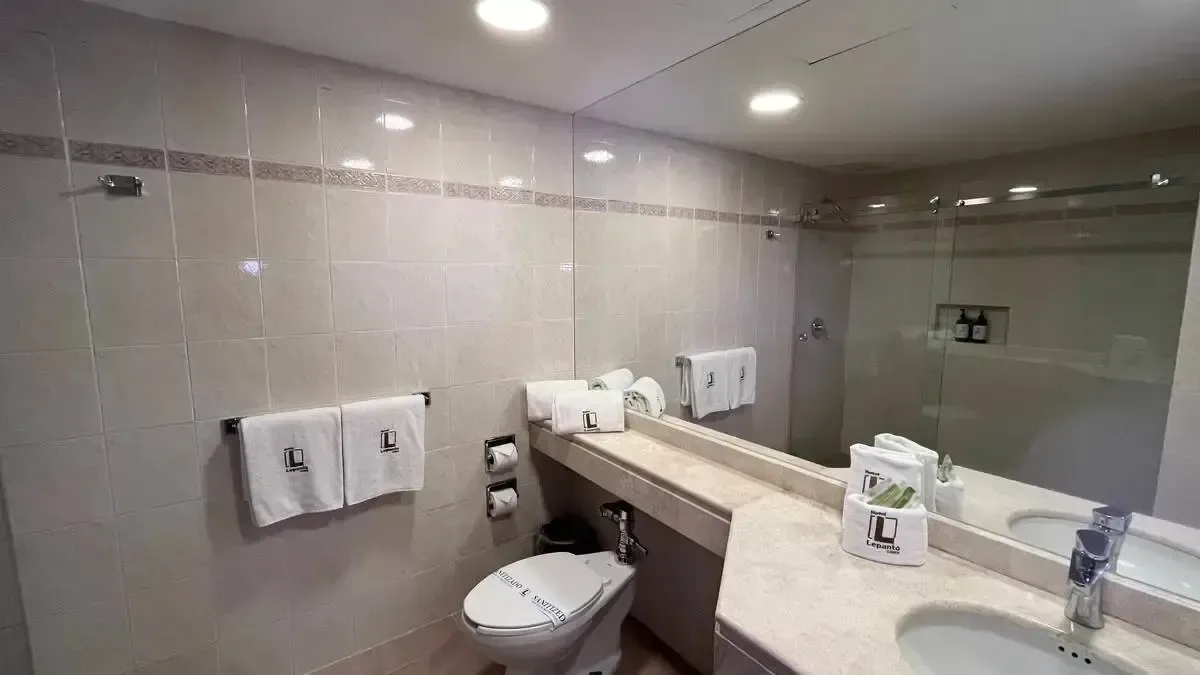 A bathroom in a hotel room with a toilet , sink and mirror.