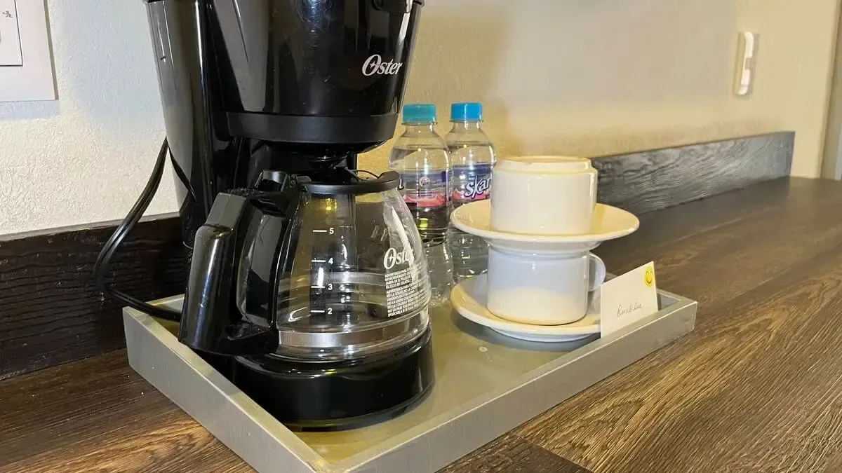 A coffee maker is sitting on a tray next to a cup and saucer.
