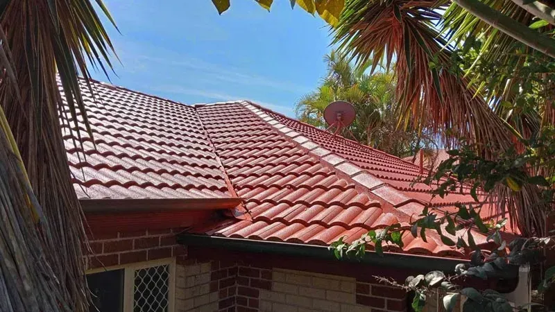 Red tile roof on a brick house, surrounded by green palm trees and a clear blue sky.