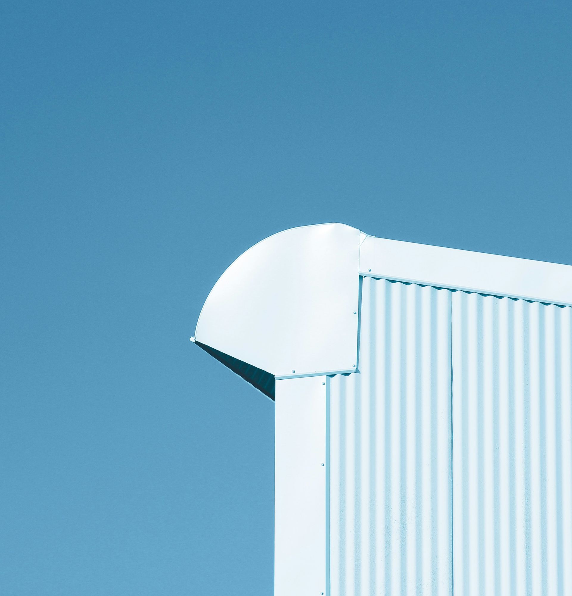 White building corner against a blue sky. Corrugated siding with rounded edge.