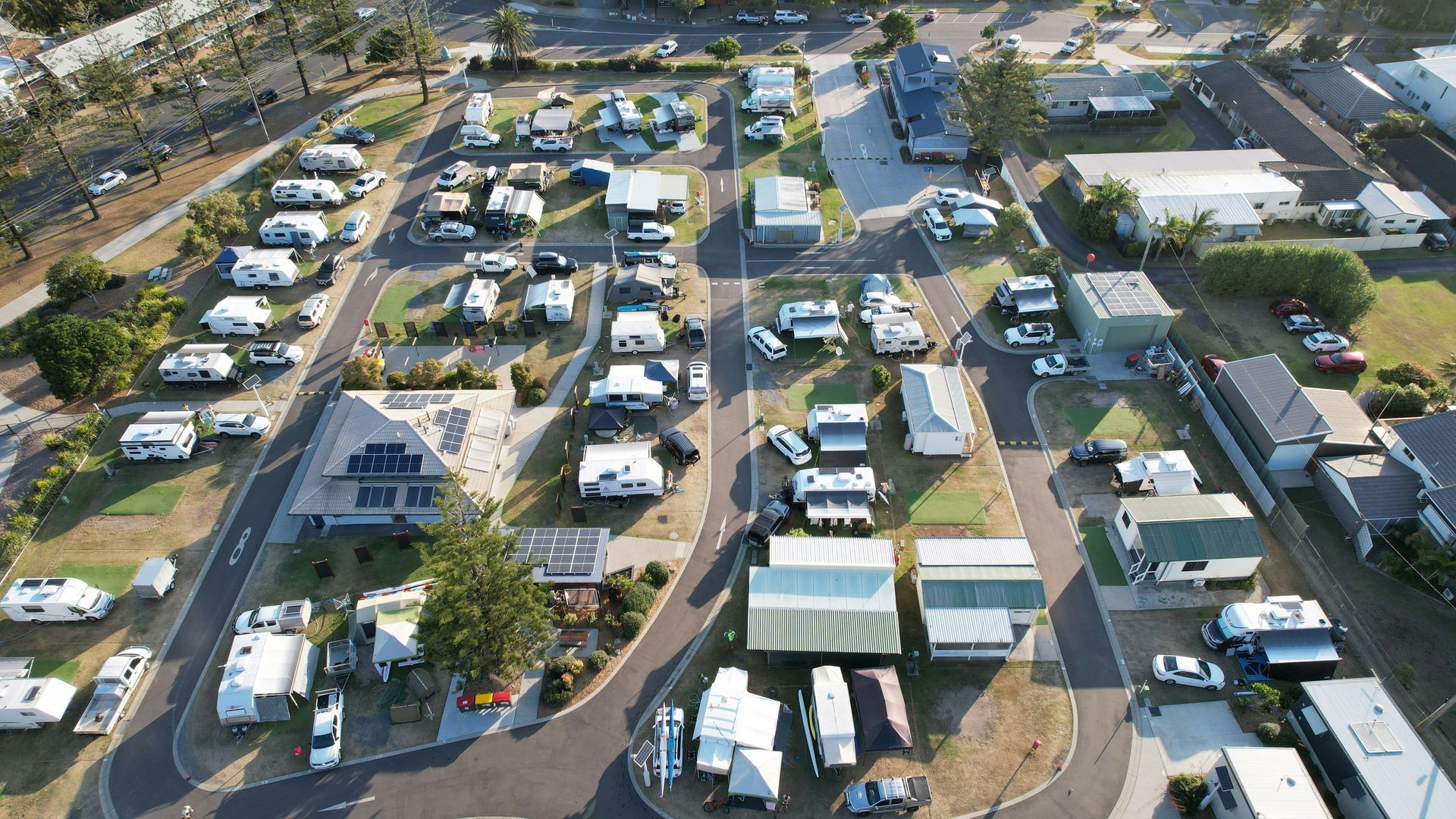 Woolgoolga - Aerial view of a caravan park with RVs and tents, surrounded by buildings and trees.