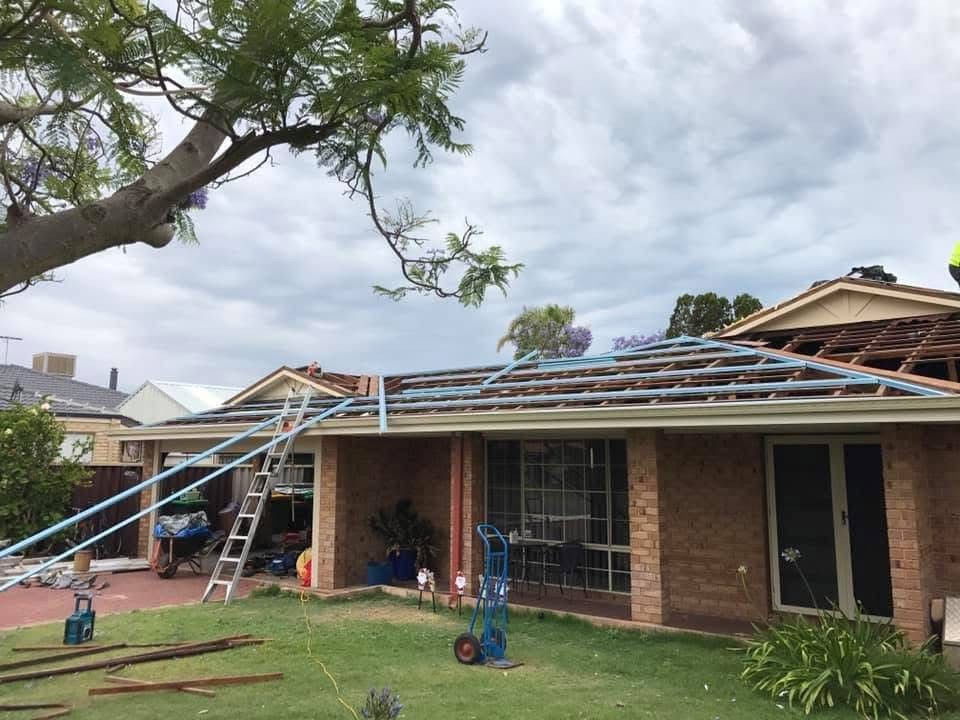 Roof of a brick house under renovation with exposed rafters. Ladder, tools, and a cloudy sky.