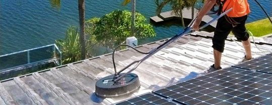 Person pressure washing a roof with solar panels next to water.
