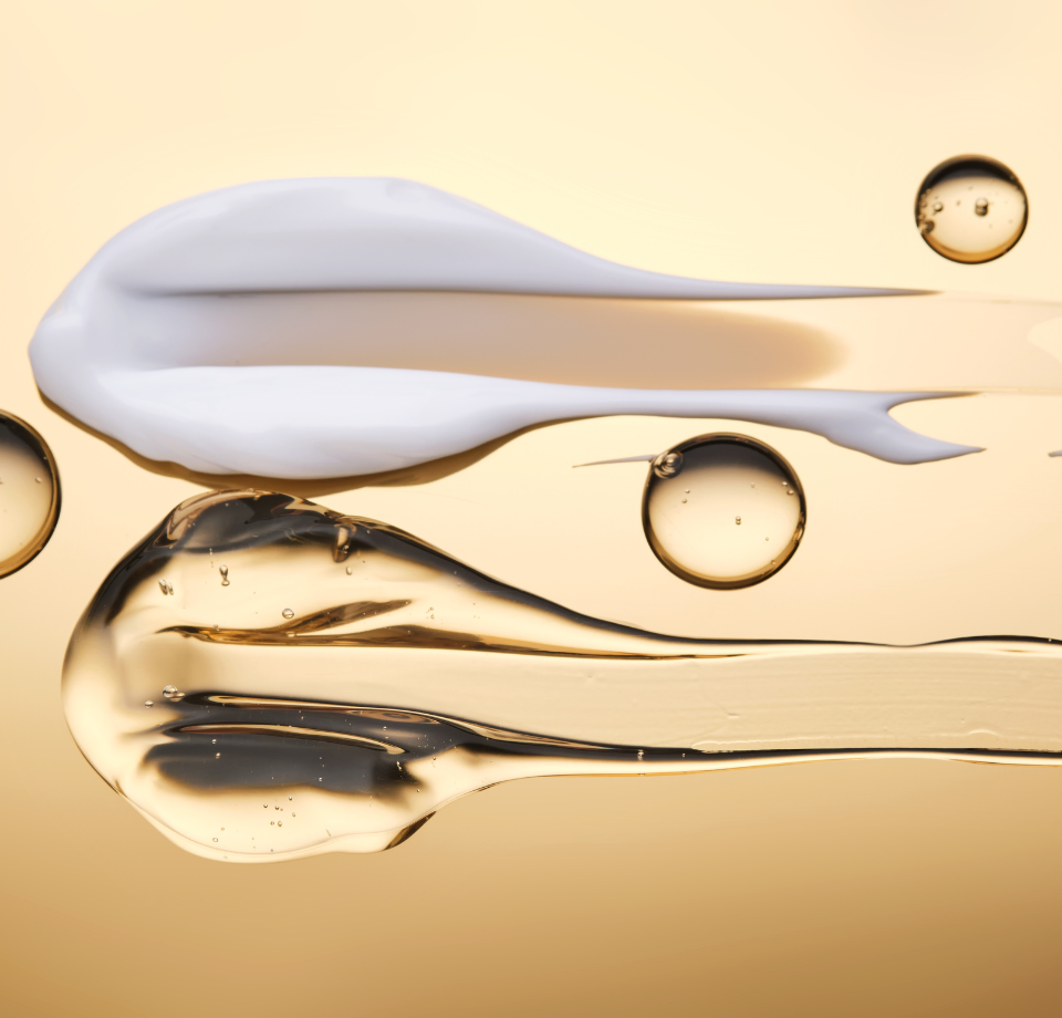 Campioni di crema bianca e gel dorato, con bolle galleggianti, su una superficie dorata.