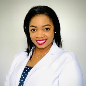 Woman in a white coat smiling, wearing a necklace. She has dark hair and red lipstick.