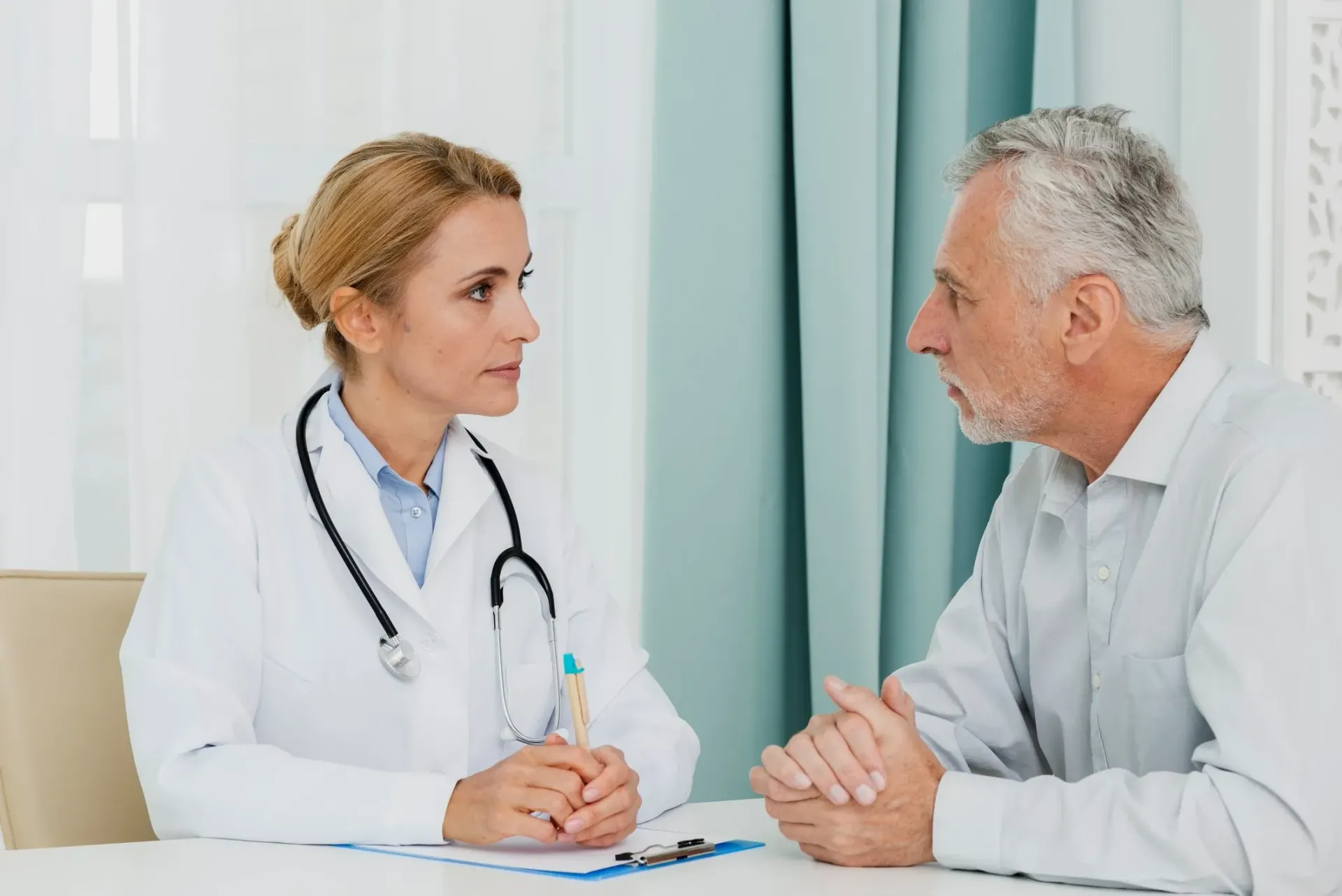 Doctor in white coat consults with a patient at a desk. The patient appears to be listening intently.