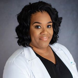 Woman in white coat, smiling, dark hair styled, soft focus background.