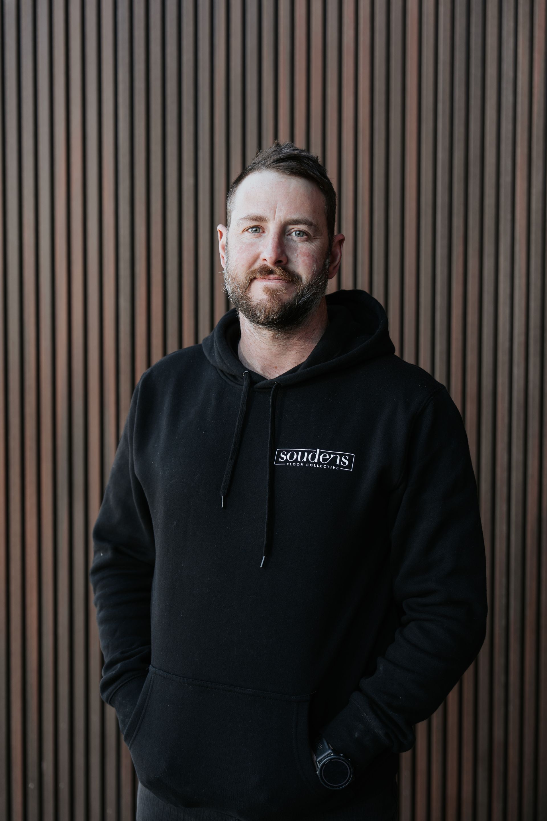 A man with a beard is wearing a black jacket and smiling for the camera.