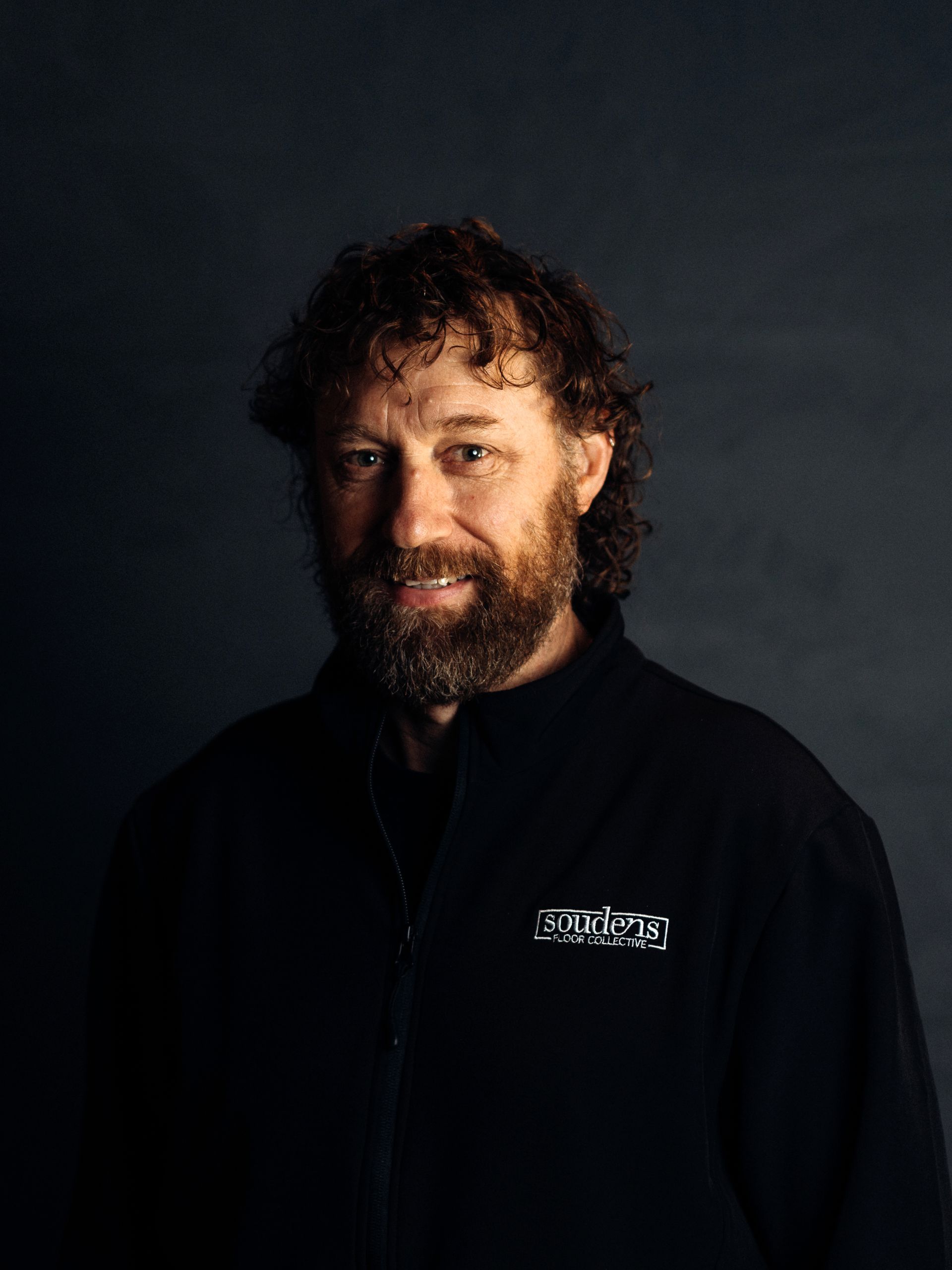 A man with a beard and curly hair is wearing a black jacket.