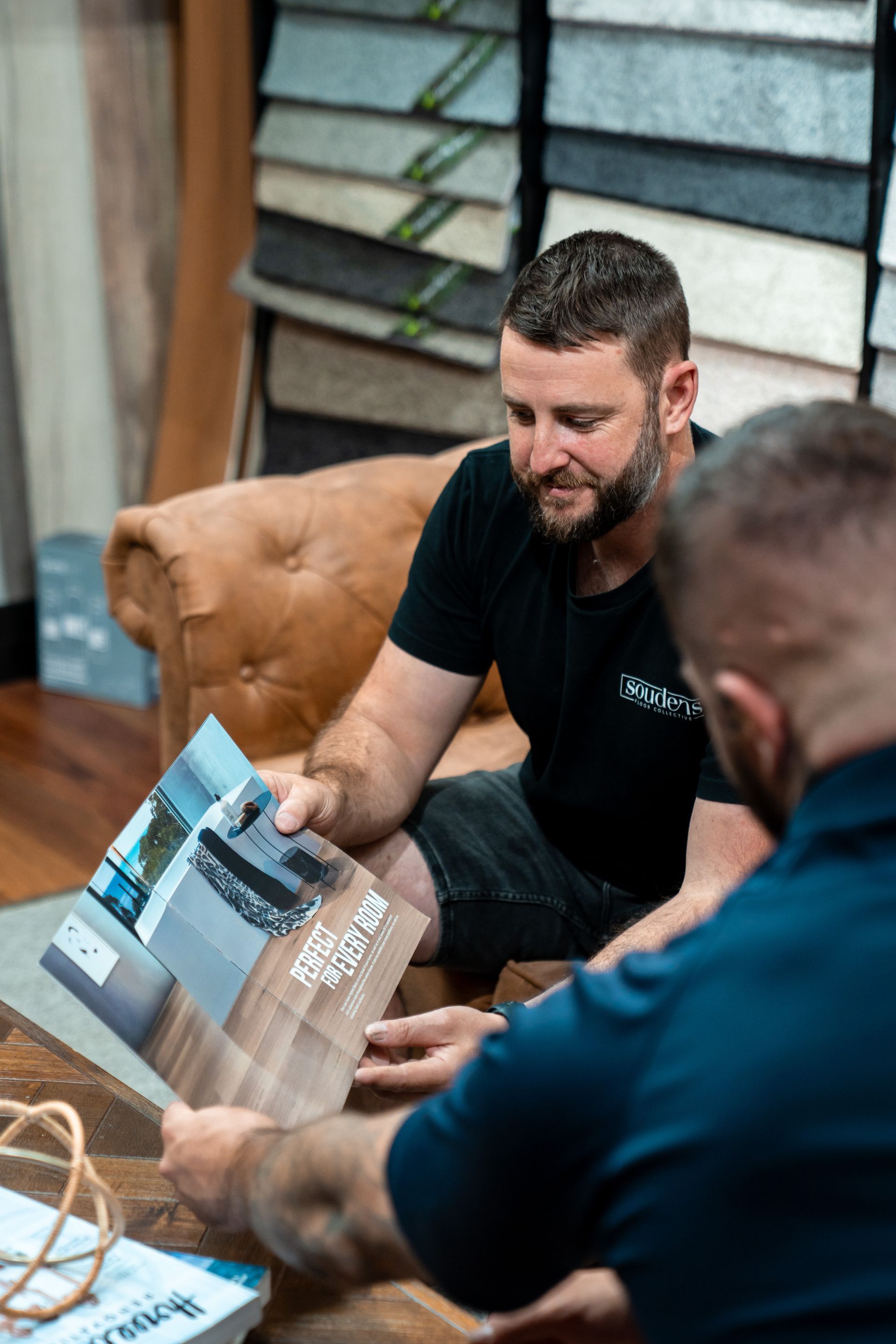 Two men are sitting on a couch looking at a brochure.