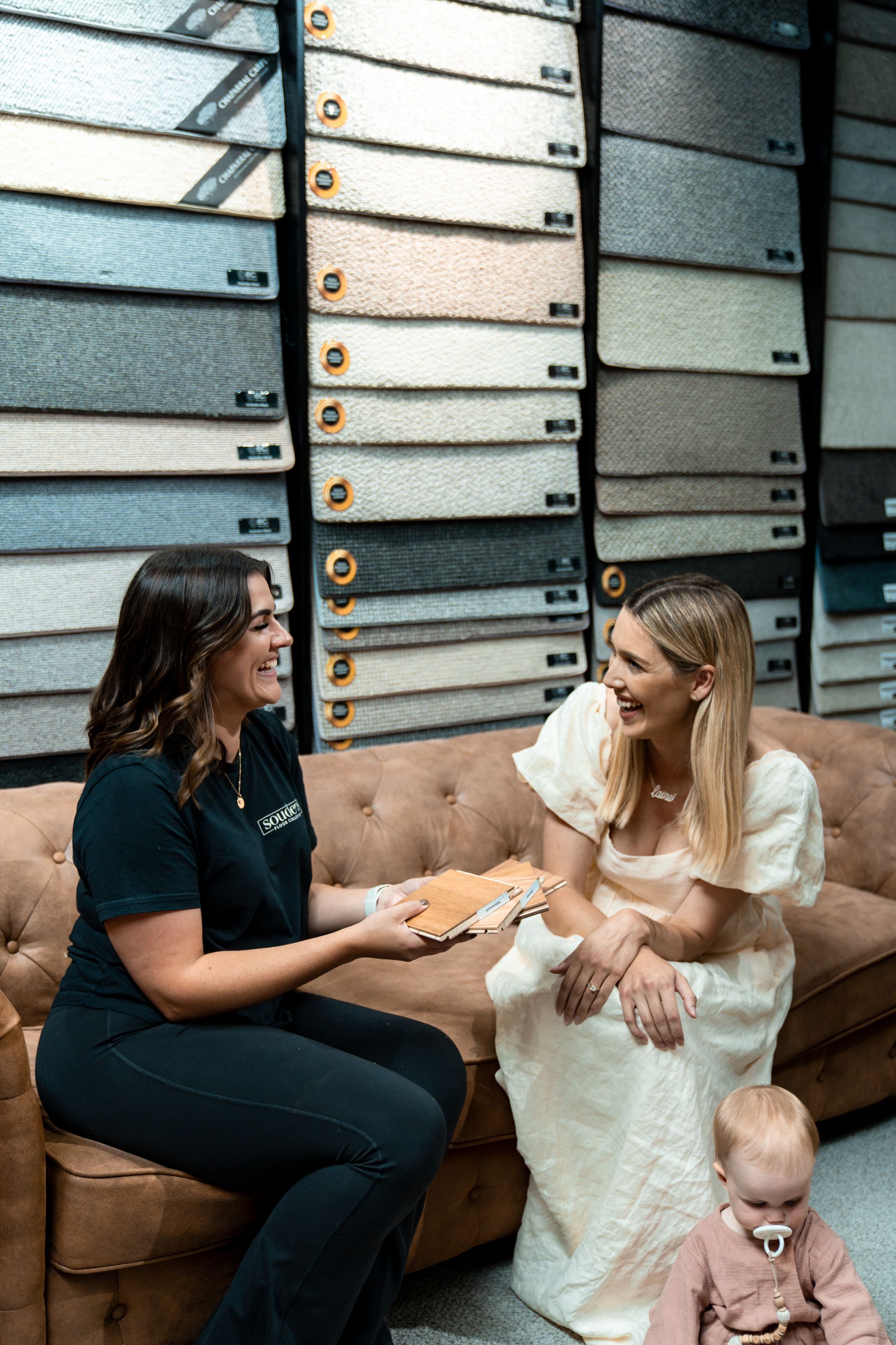 A woman is sitting on a couch talking to another woman and a baby.