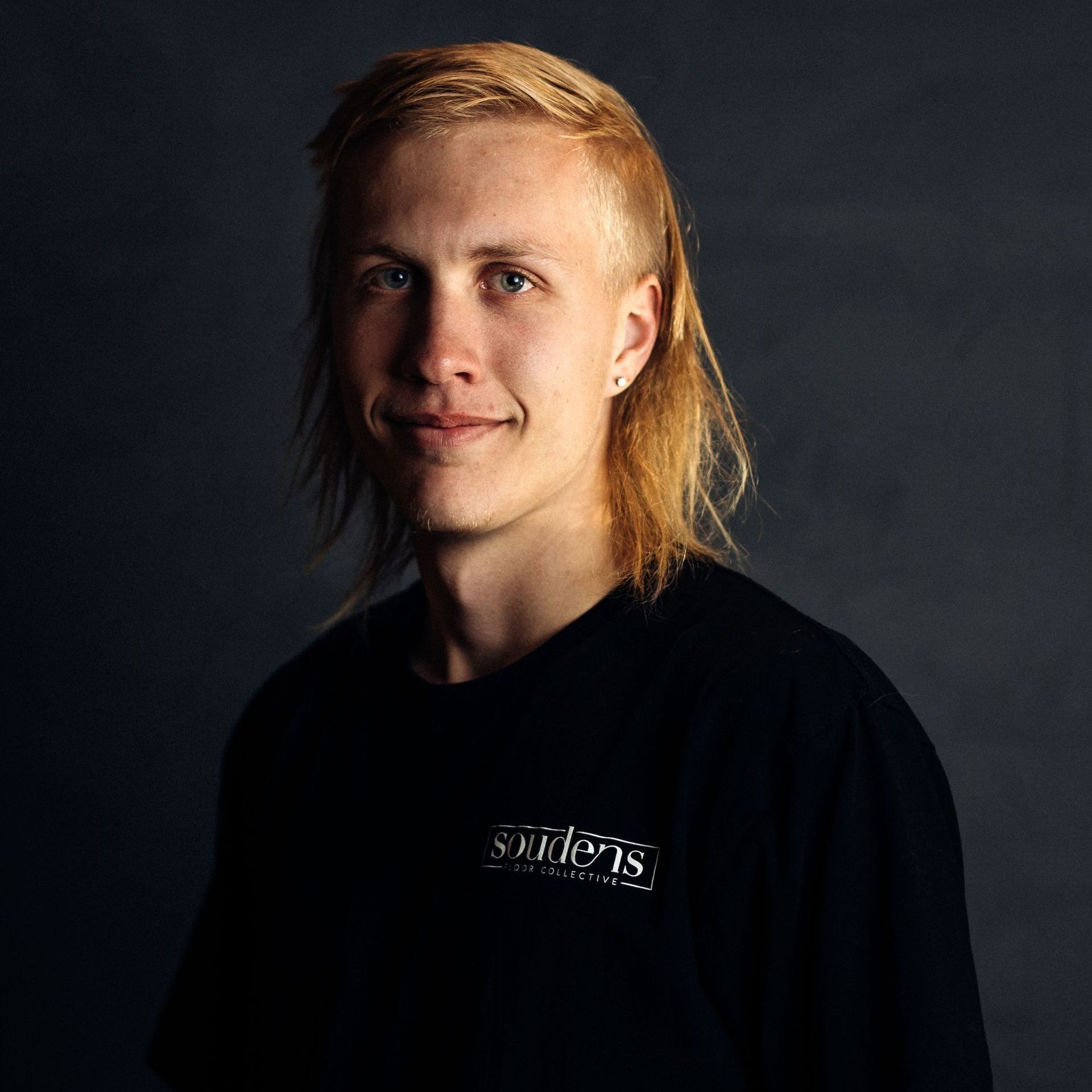 A young man with long blonde hair is wearing a black t-shirt.