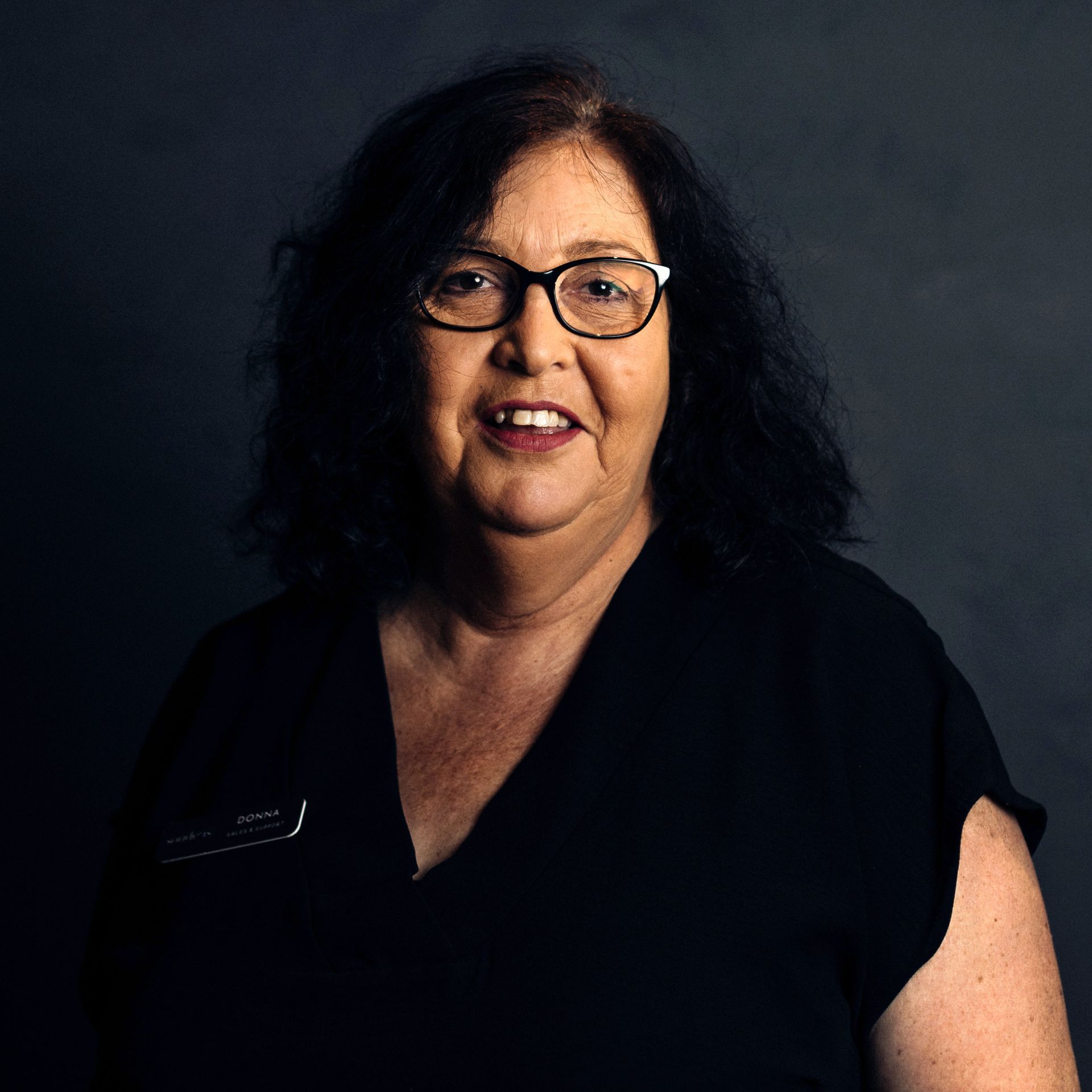 A woman wearing glasses and a black shirt is smiling for the camera.