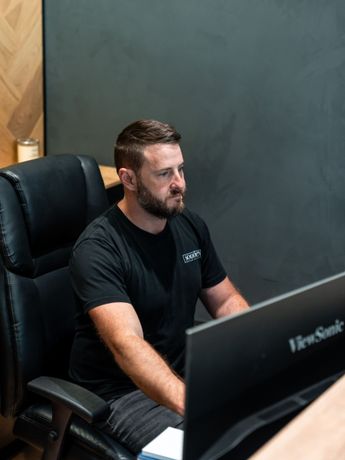 A man in a black shirt is sitting in front of a computer monitor.
