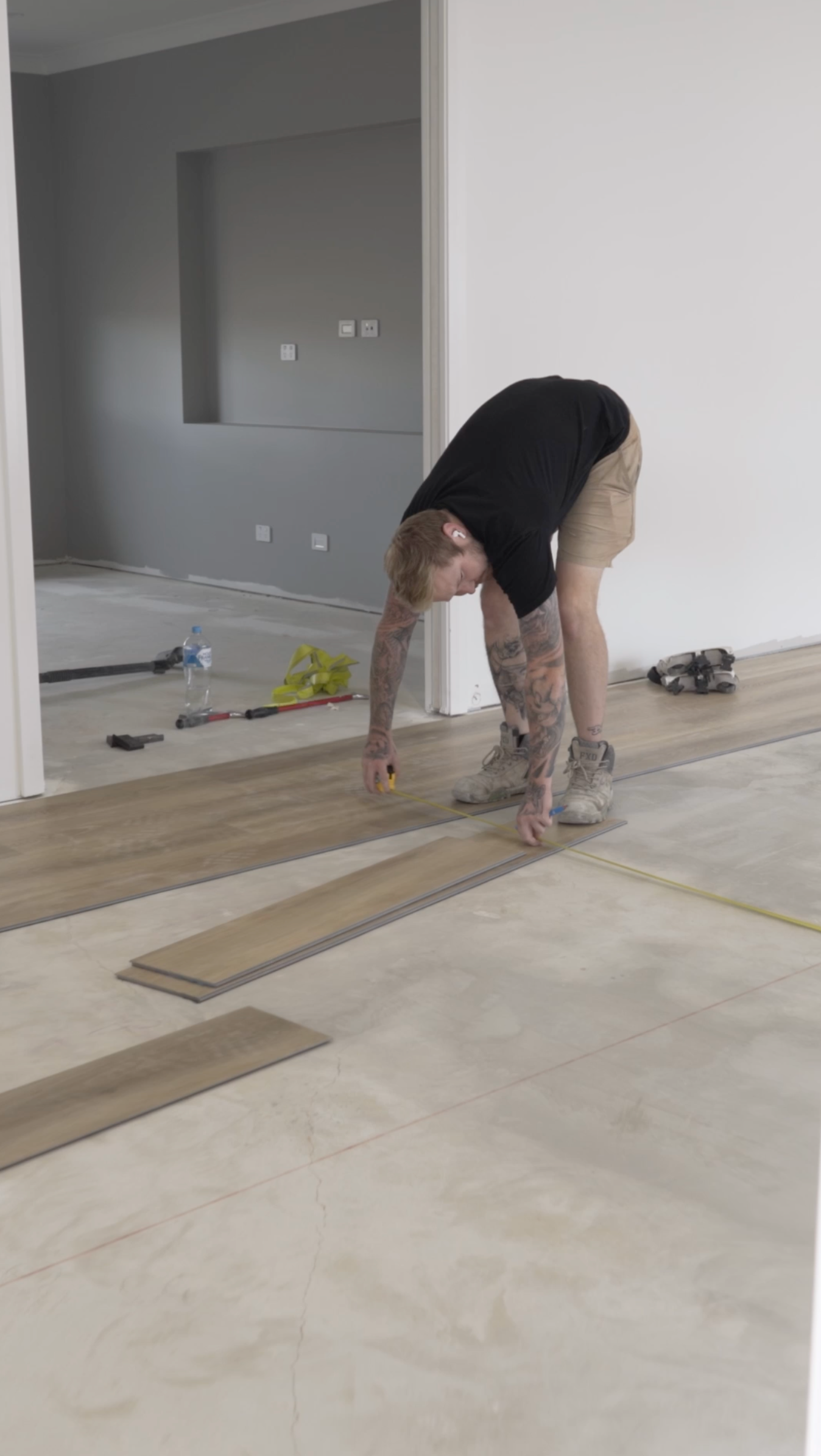 A man is bending over to measure a piece of wood on the floor.