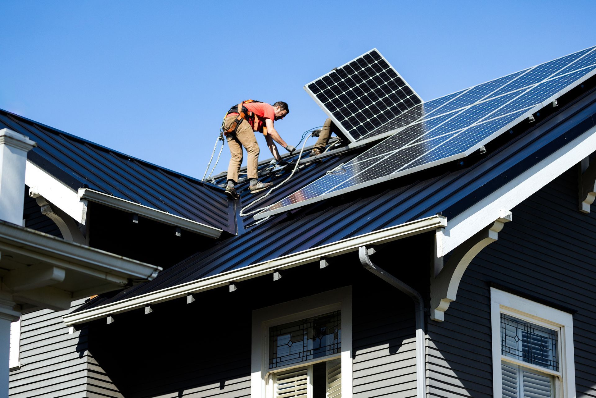 A man is installing solar panels on the roof of a house