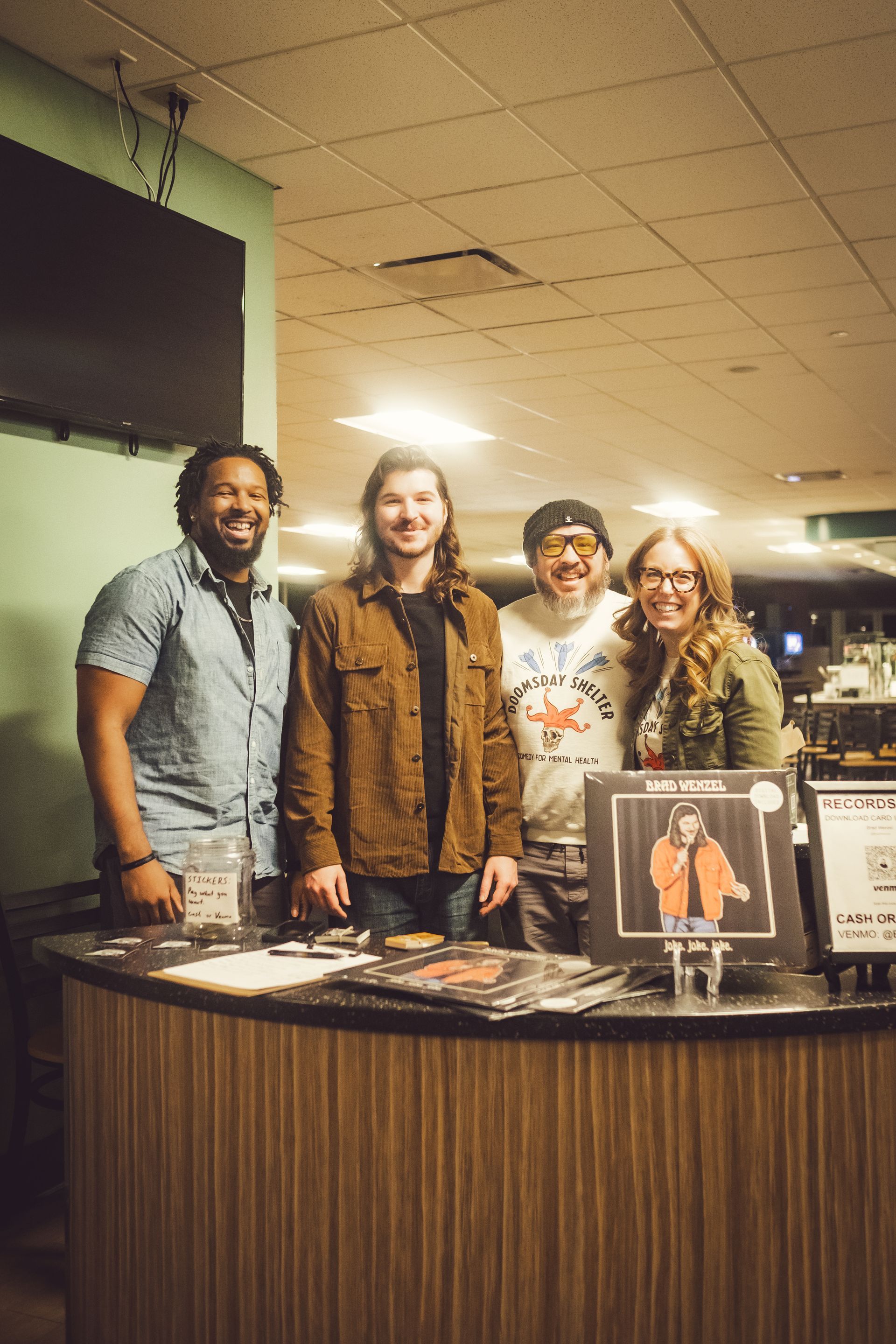 Four people posing behind a table with vinyl records; one woman is smiling, others look at the camera.